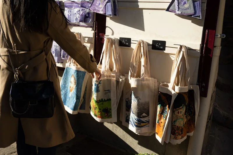 Woman shopping for art-printed tote bags at a market, showing the lifestyle appeal of artist designs on products
