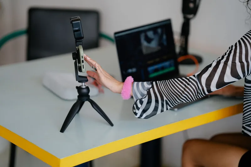 Woman adjusting smartphone on tripod with laptop setup for content creation