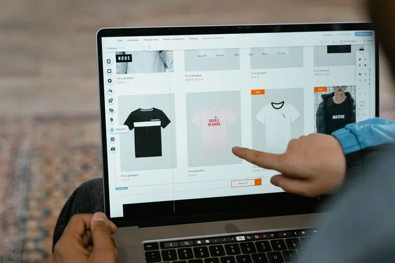 Hand pointing at a product listing in a storefront catalog grid on a laptop screen, representative of browsing a beat marketplace page