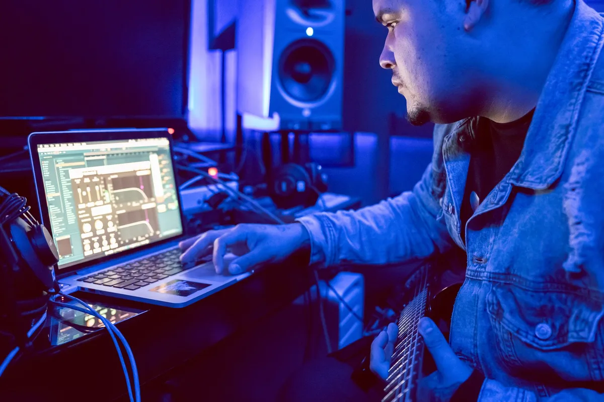 Musician working on a laptop in a home studio setup with headphones and audio equipment