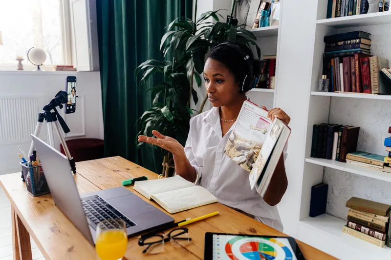 Woman teaching an online lesson on a laptop with a phone tripod recording her