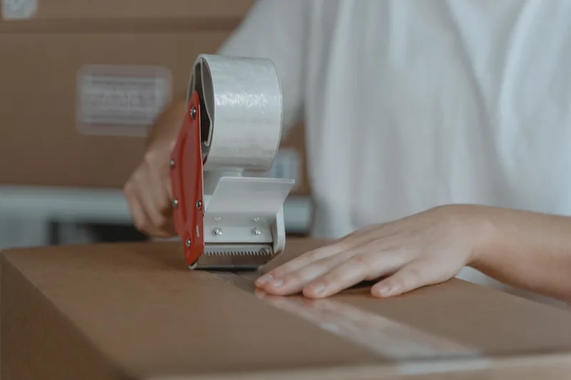 Close-up of hands sealing a cardboard shipping box with packing tape