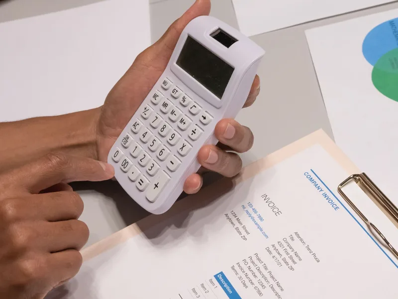Close-up of hands using a calculator next to a company invoice on a desk